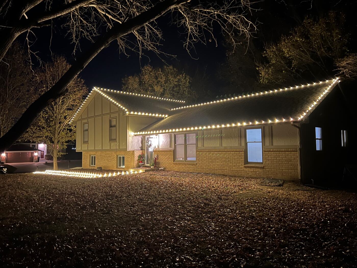 Brick home with warm white roofline lighting beneath bare trees